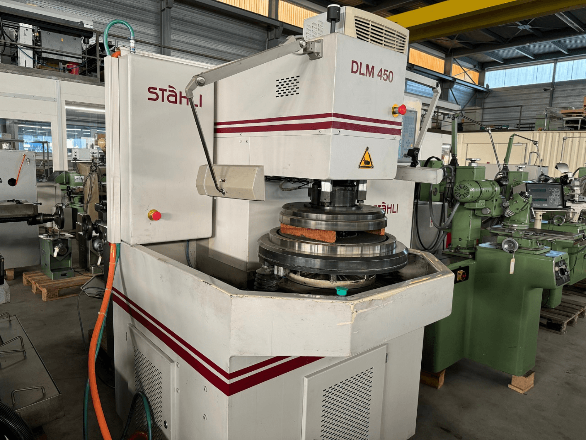 Плоскошлифовальный станок STAEHLI DLM 450, вид спереди с шлифовальным кругом и панелью управления, в промышленной обстановке.