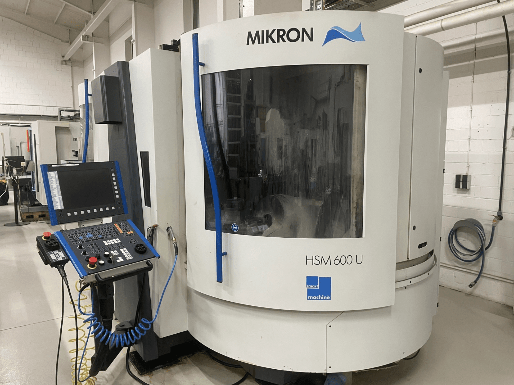 Вертикальный обрабатывающий центр MIKRON HSM600U, показанный спереди, с оперативной панелью управления и большим смотровым окном.
