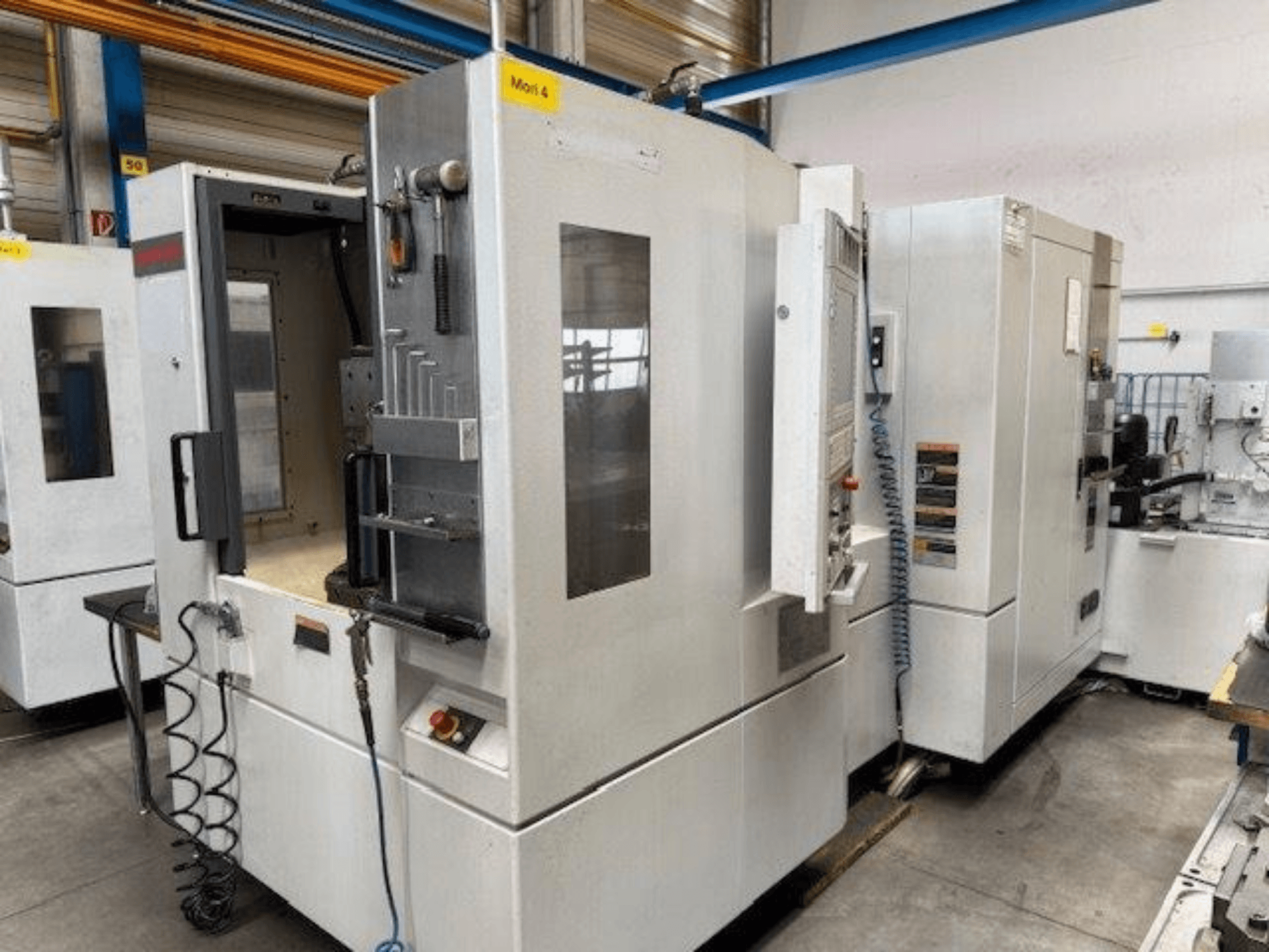 Горизонтальный обрабатывающий центр MORI SEIKI NH4000 DCG, показанный спереди, с открытой дверью и деталями панели управления.