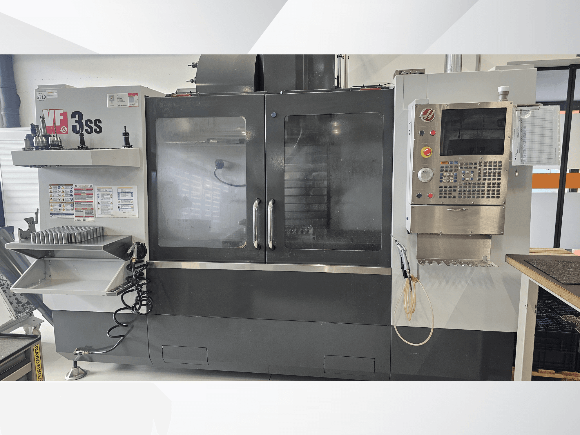 Вертикальный обрабатывающий центр HAAS VF-3SS, вид спереди, панель управления, стойка для инструментов и большая стеклянная дверь.