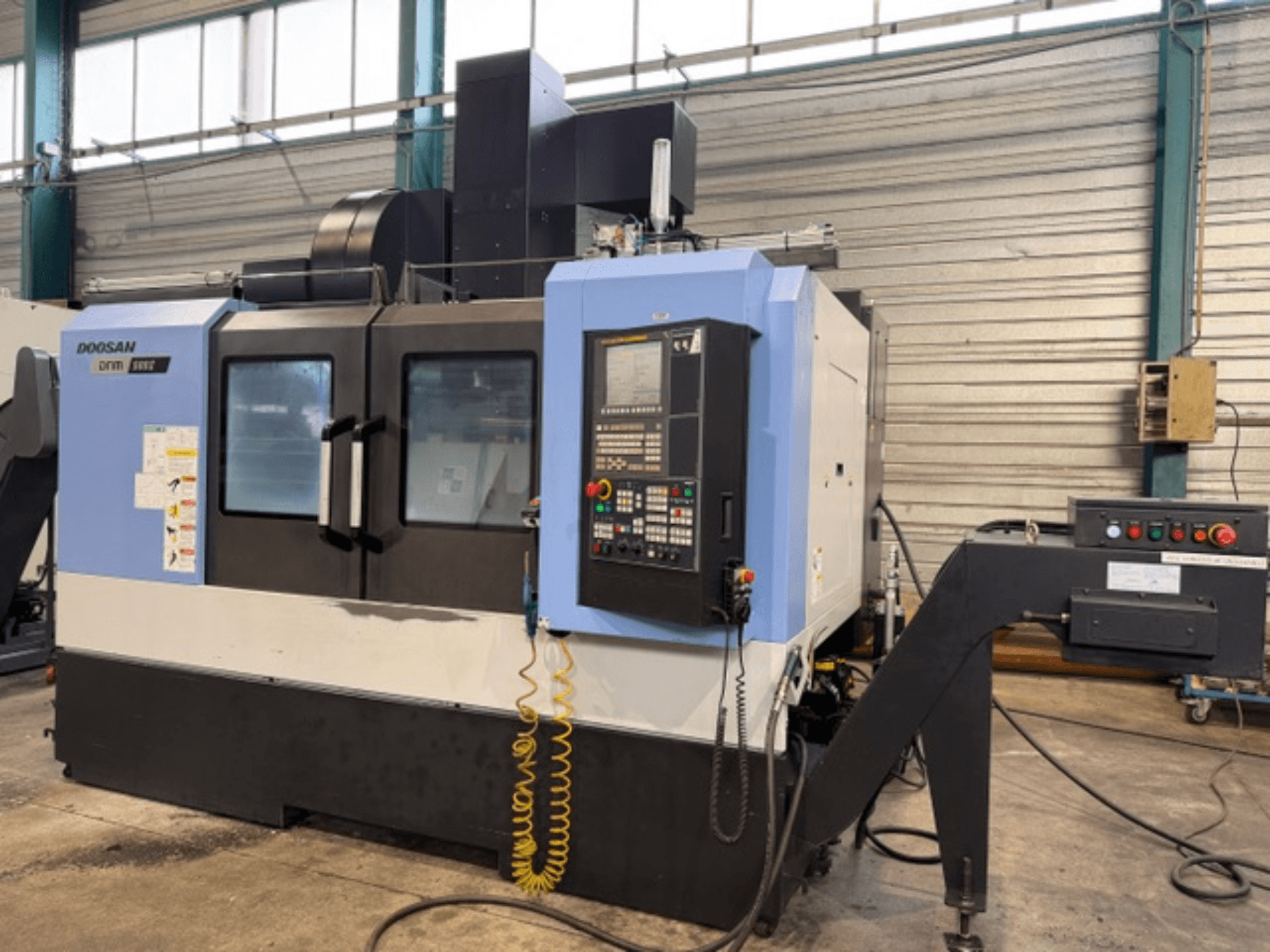 Фрезерный станок с ЧПУ Doosan DNM 500II с видом спереди, с панелью управления и держателем инструмента, в заводских условиях.