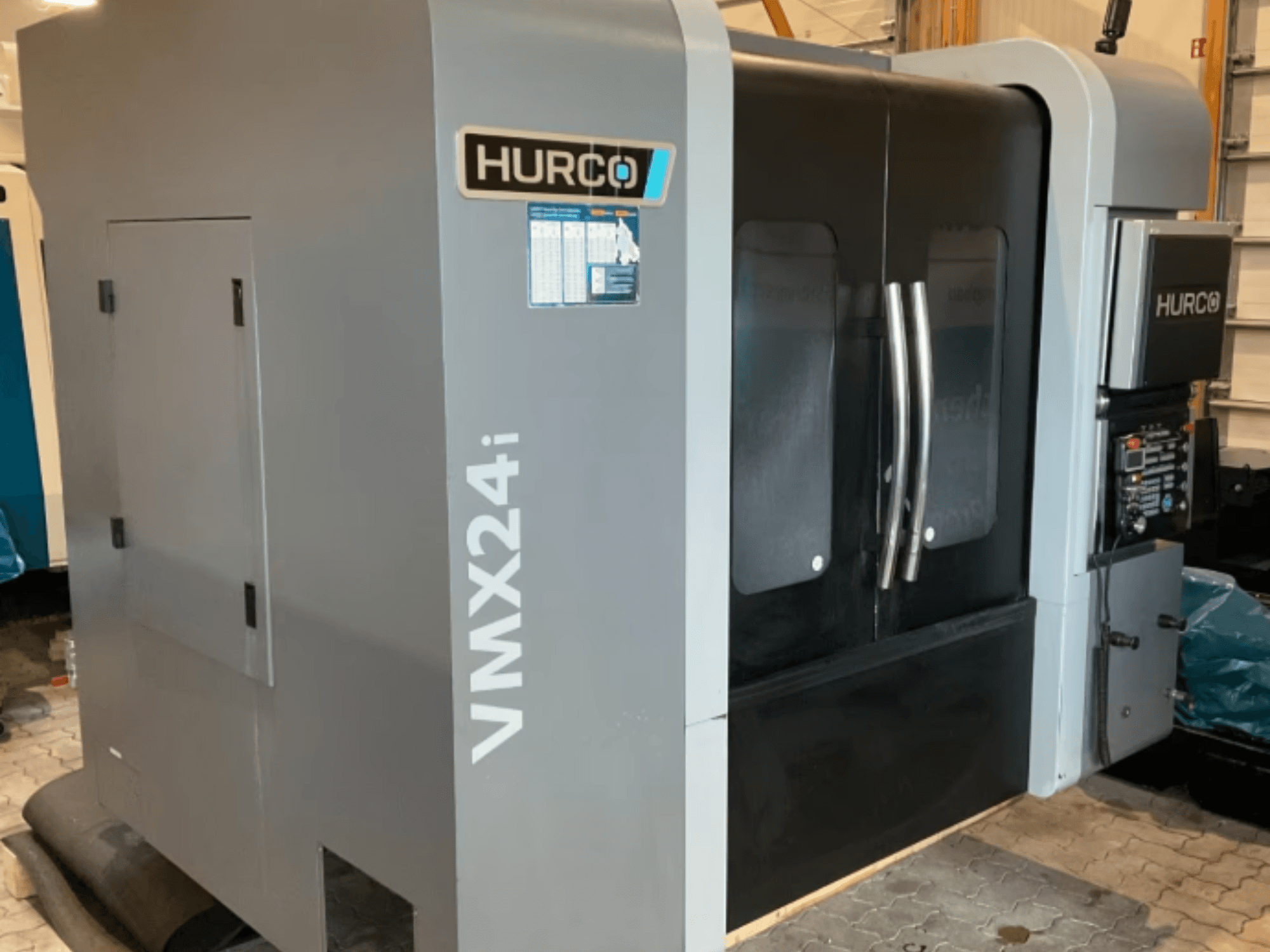 Вертикальный обрабатывающий центр Hurco VMX 24i, вид спереди: корпус металлического серого цвета, черные дверцы панелей и интерфейс управления.