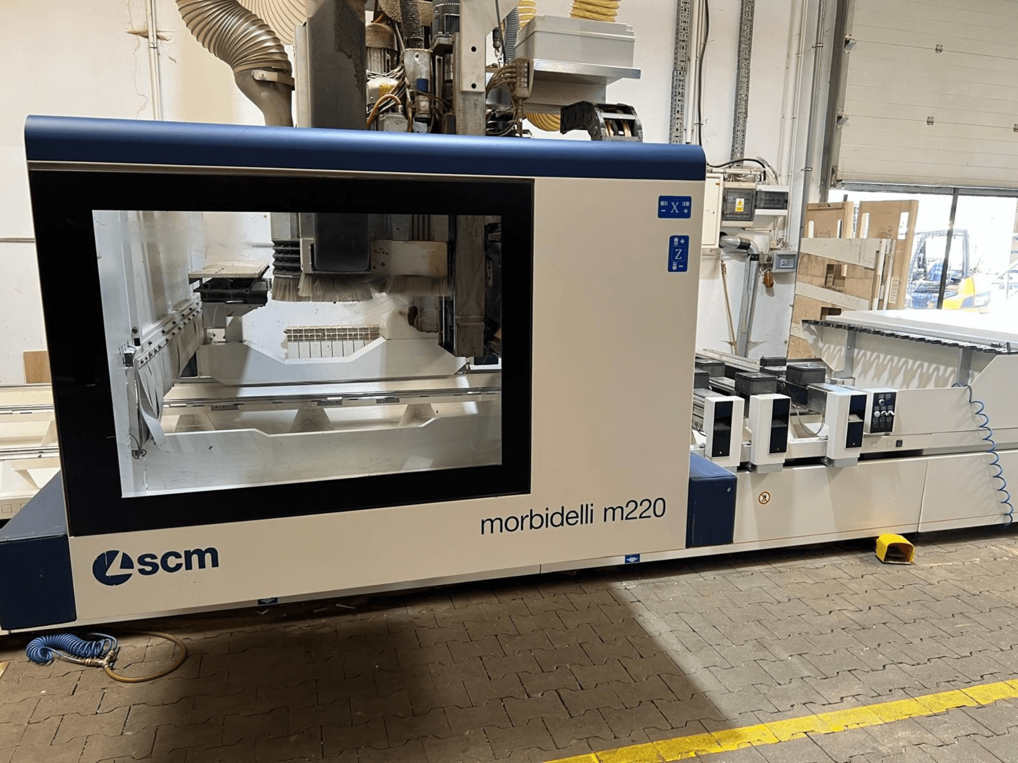 Вид спереди на обрабатывающий центр с ЧПУ SCM Morbidelli M220, на котором видны большое окно, панель управления и рабочая зона.