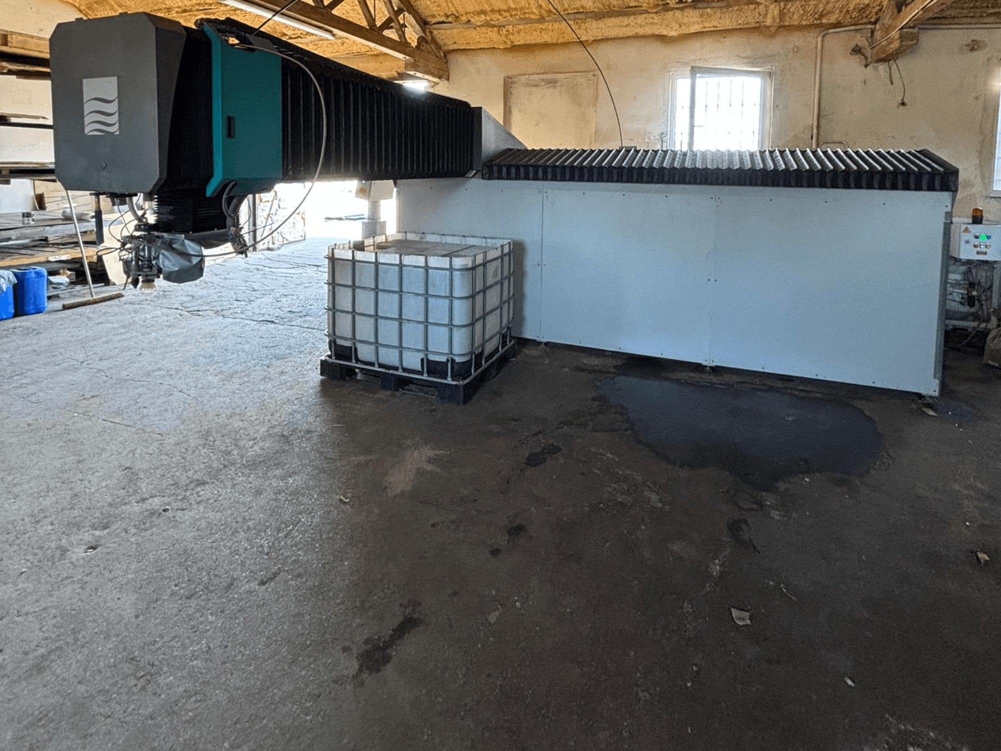 Промышленный водоструйный аппарат в мастерской, вид сбоку, рядом с ним видны большой бак для воды и панель управления.