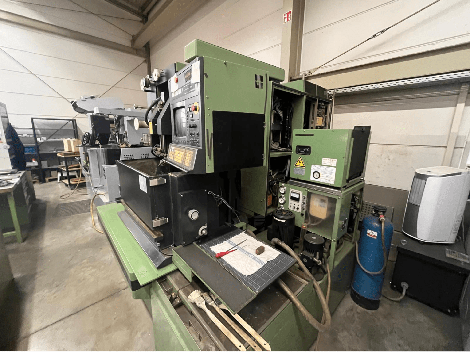 Зеленый промышленный станок с панелью управления, вид сбоку; включает гидравлические компоненты и рабочую поверхность с инструментами.