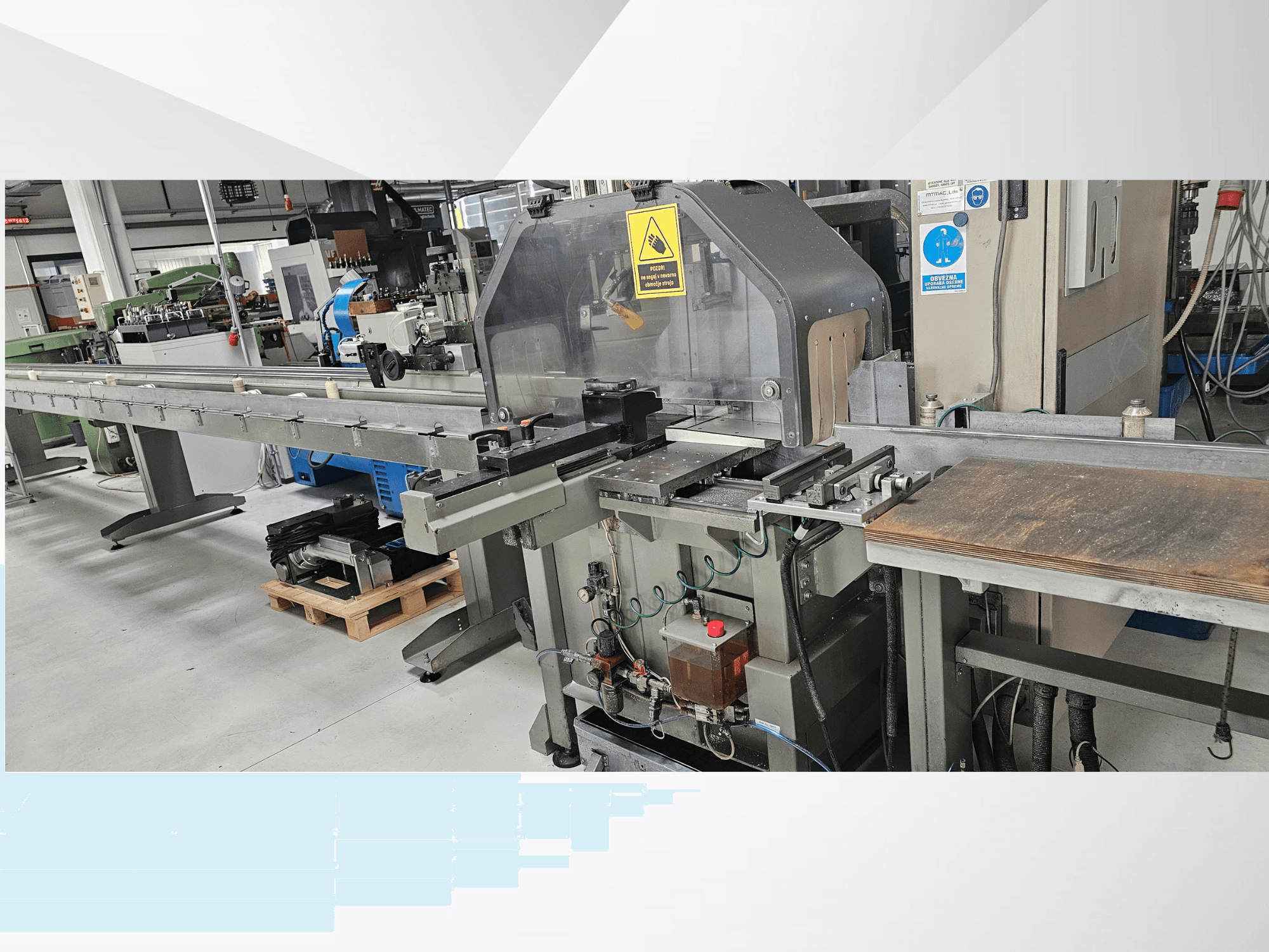 Промышленный раскройный станок с видом сбоку, с длинным конвейером, панелью управления и предупреждениями о безопасности.