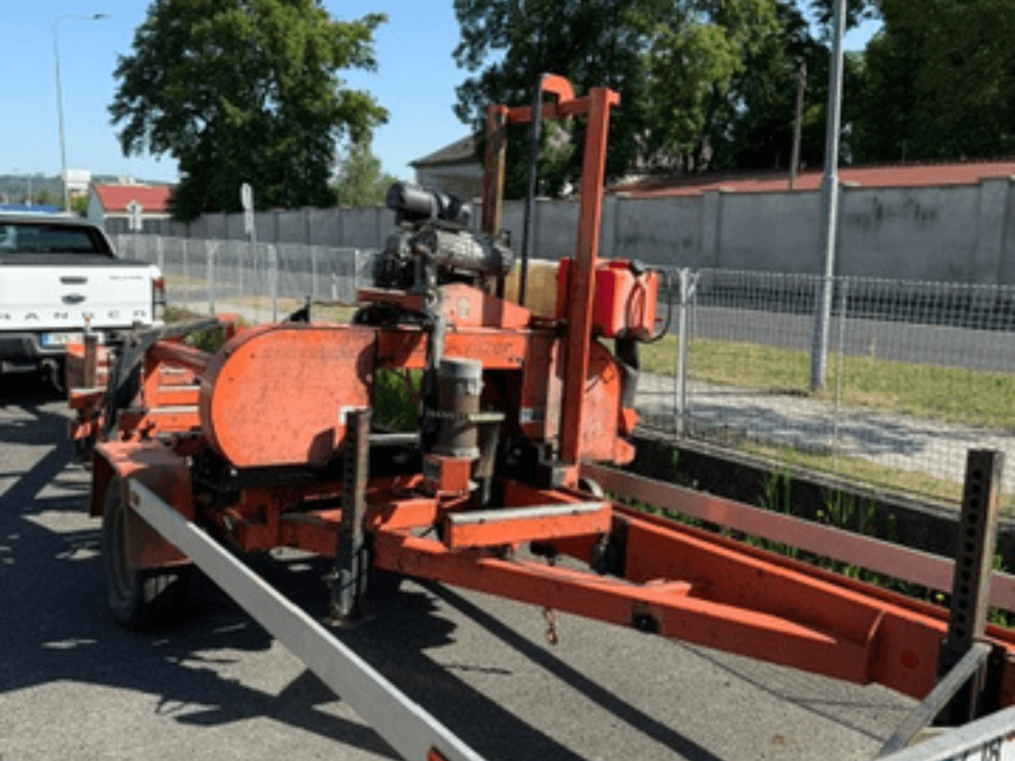 Ленточная пила для резки древесины WOOD-MIZER LT40 оранжевого цвета, вид сбоку на прицепе с видимыми колесами и деталями двигателя.