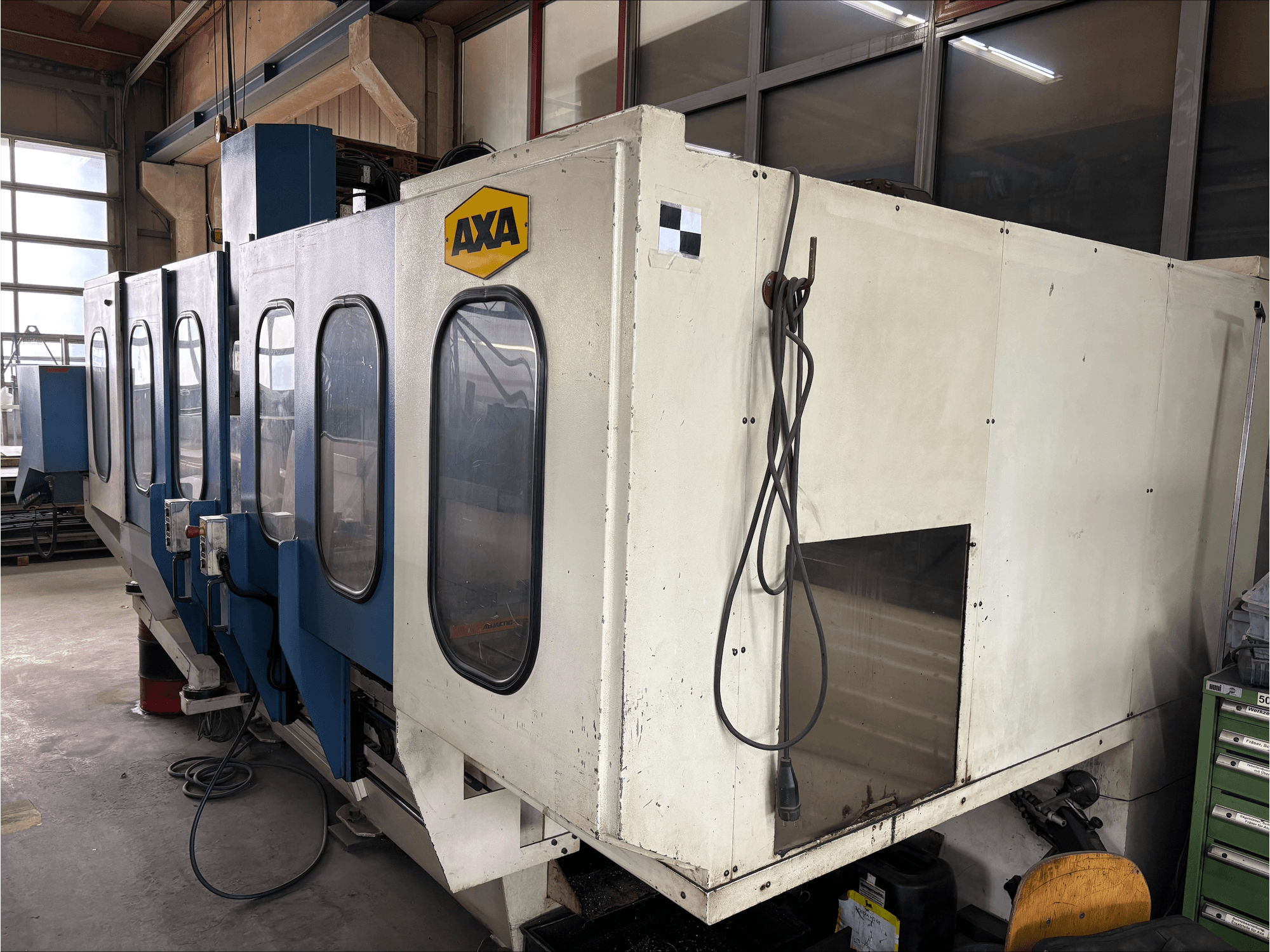Вертикальный обрабатывающий центр AXA VSC-1-M/C, вид спереди, большой белый шкаф и синяя панель управления.