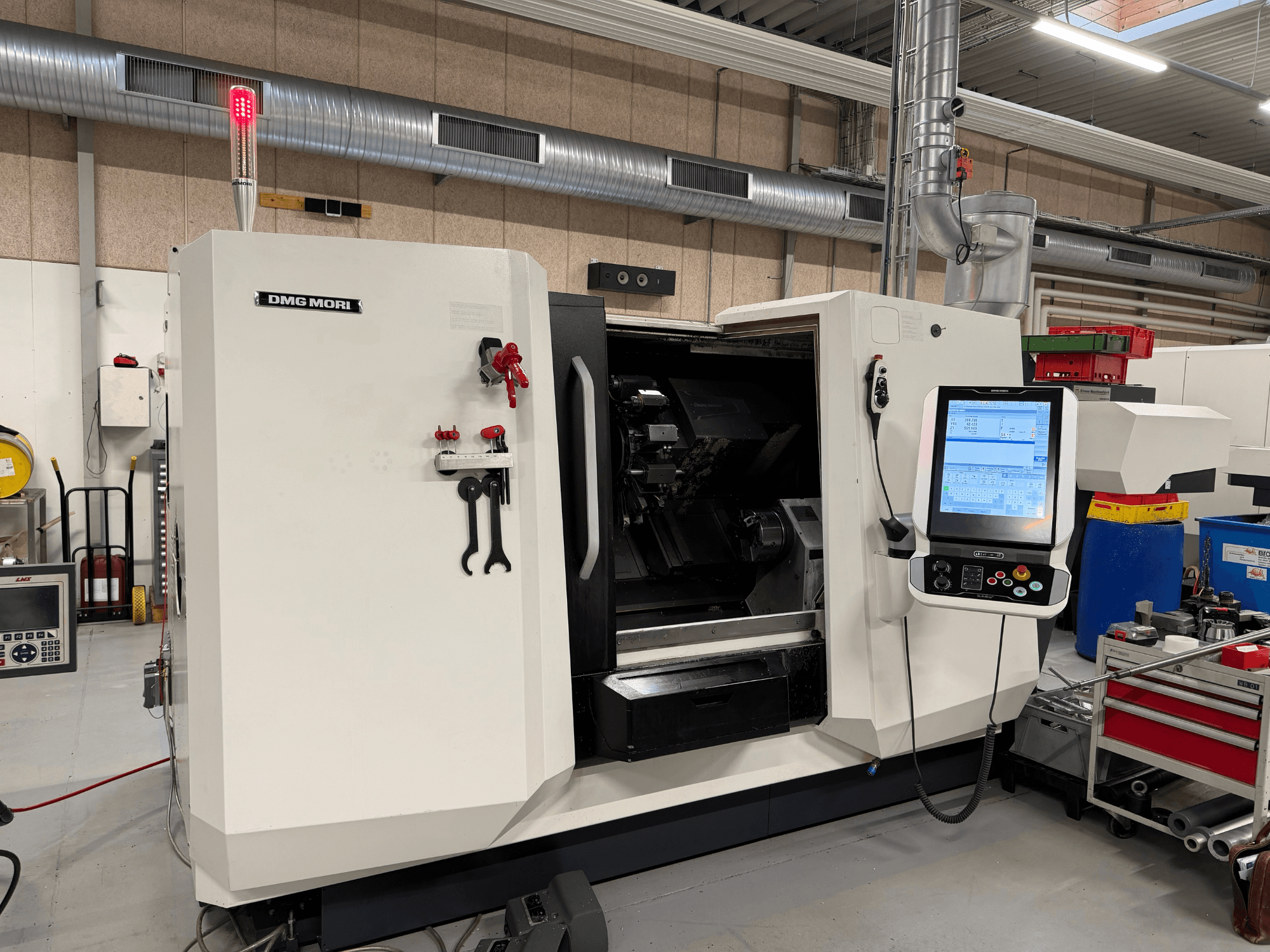 Горизонтальный токарный станок DMG MORI CLX 450 V6, вид спереди: видны панель управления, кнопка аварийной остановки и сигнальная лампа безопасности.