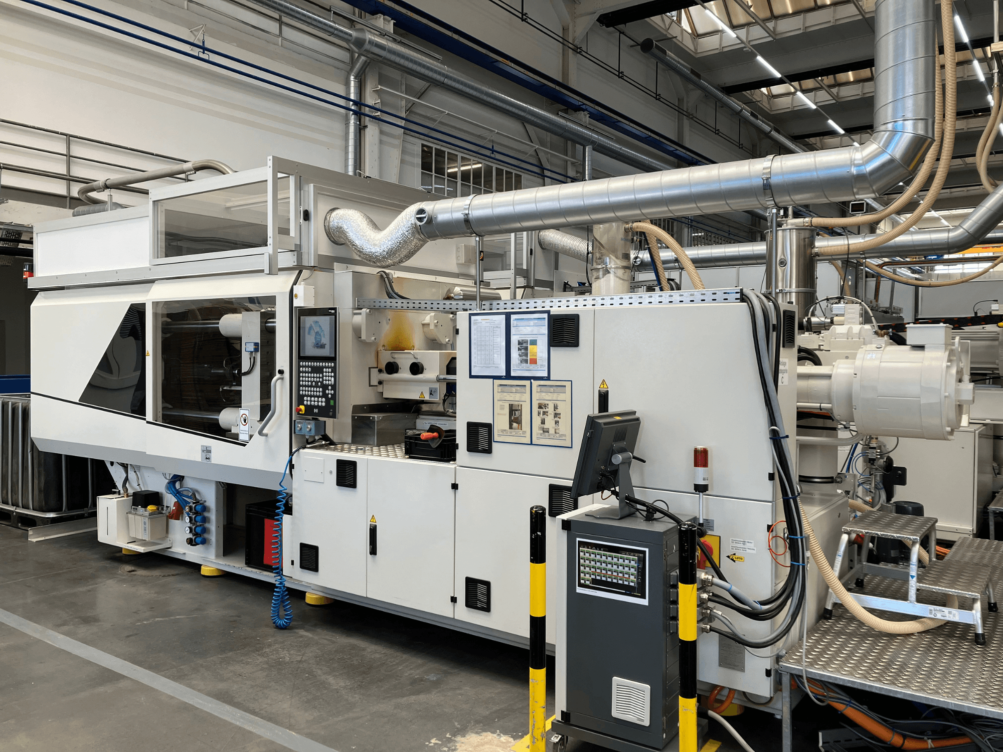 Вид спереди на промышленную машину с панелью управления, трубами и экранами дисплея, с элегантным белым дизайном и техническими деталями.