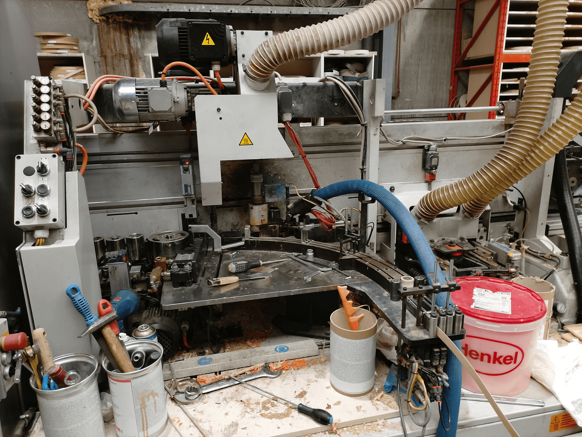 Кромкооблицовочный станок BIESSE Edge Stram B1 спереди, на фоне стружки видны механизмы, шланги и рабочие инструменты.