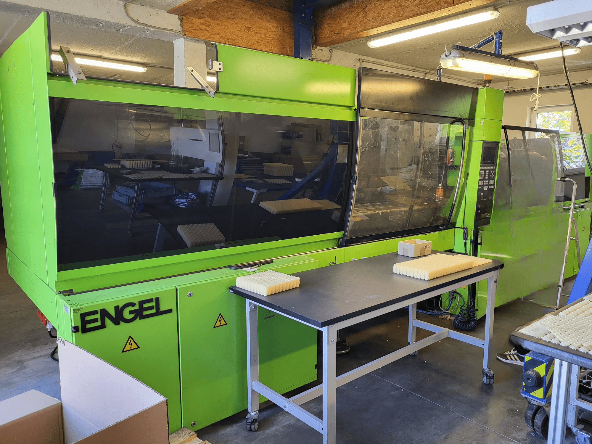 Гидравлическая термопластавтомат Green Engel ES1800/300HL, вид спереди, с материалами, уложенными стопками на рабочем столе.