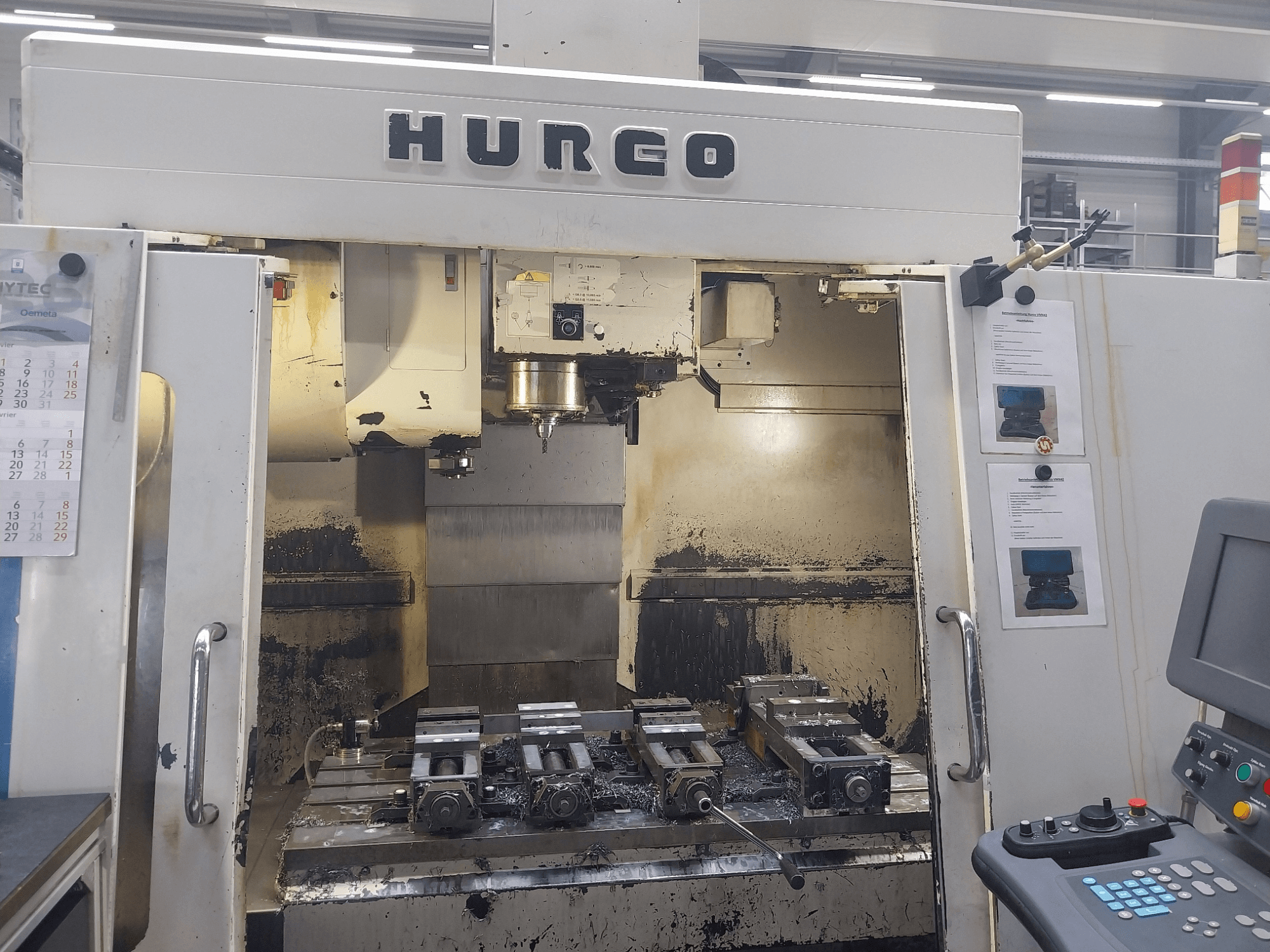 Вертикальный обрабатывающий центр Hurco VMX 42 вид спереди, рабочий стол с приспособлениями и панель управления, состояние слегка изношенное.