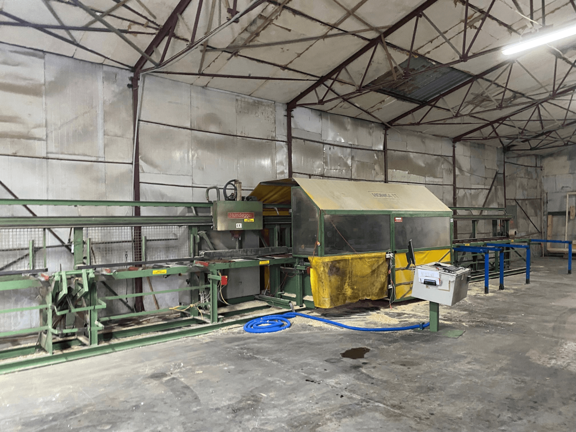 Деревообрабатывающий центр с ЧПУ HUNDEGGER K1 в мастерской, вид сбоку на станки, элементы управления и опилки на полу.