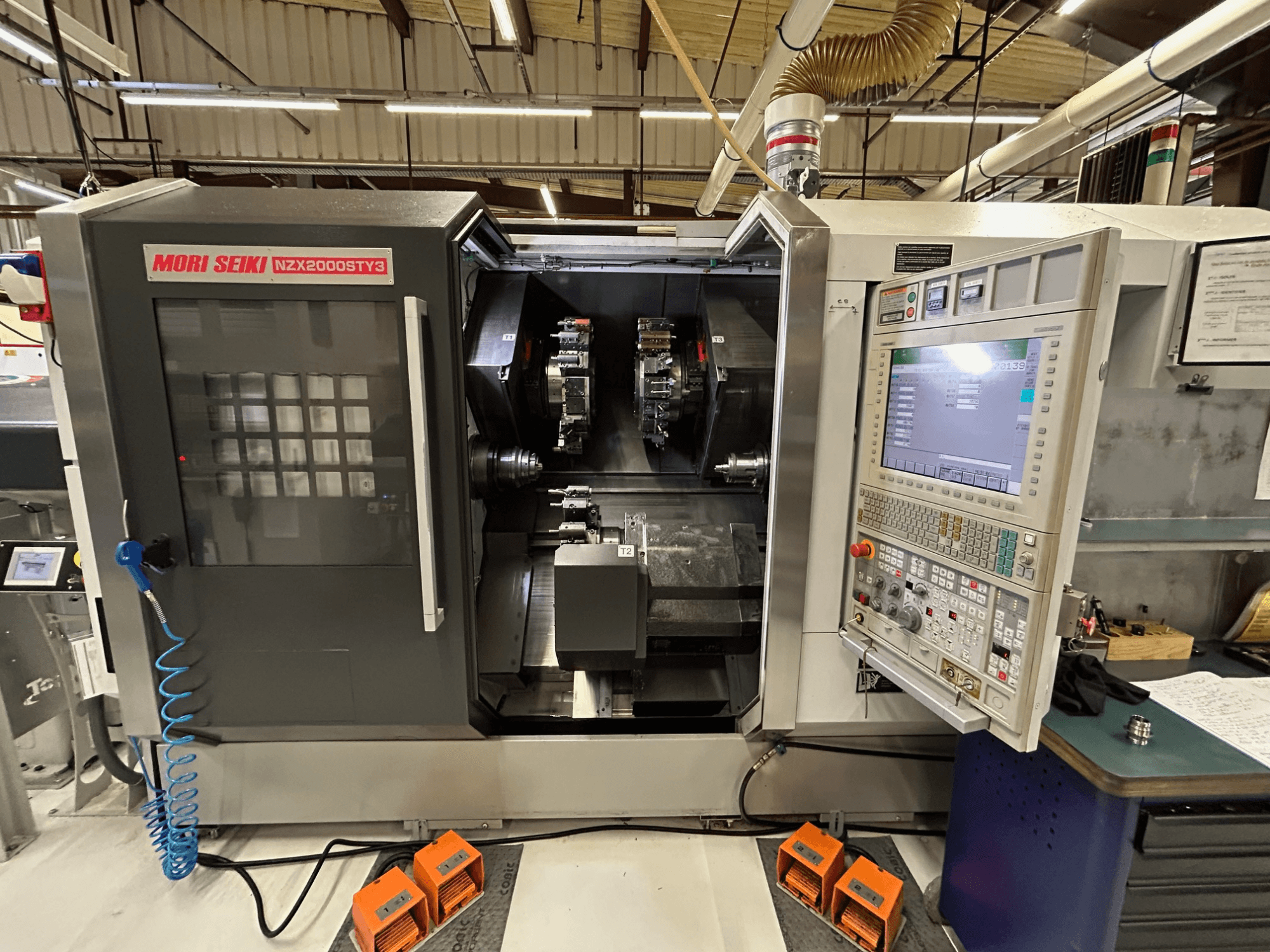 Многошпиндельный токарный станок MORI SEIKI NZ2000 ST3Y3, вид спереди с панелью управления и зоной обработки.