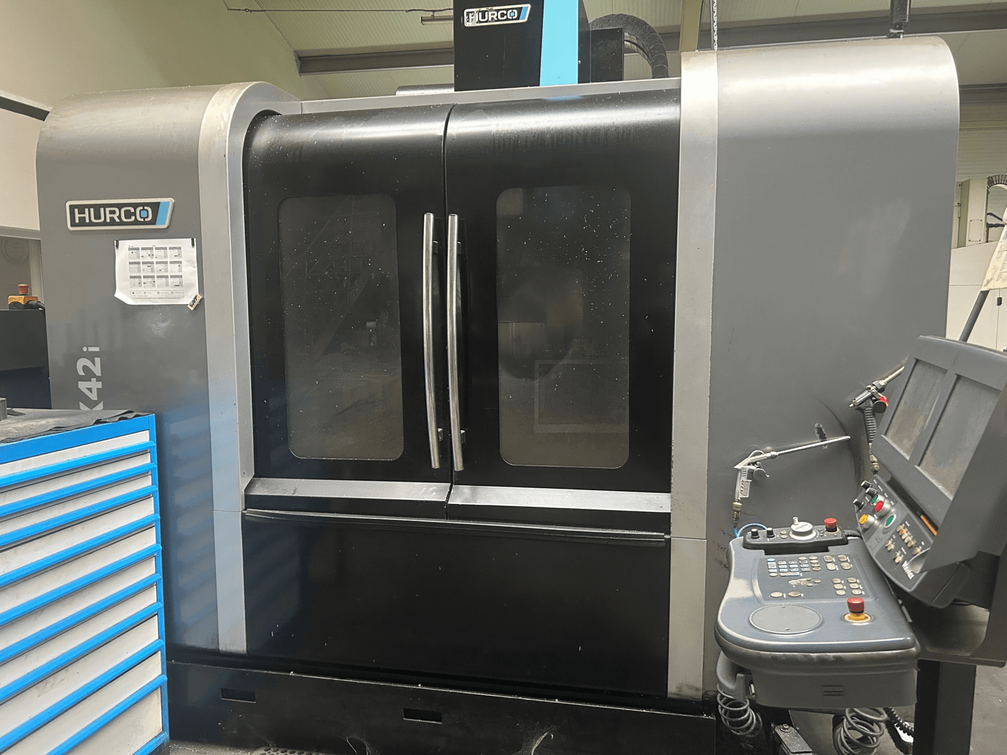 Станок с ЧПУ Hurco VMX42i, вид спереди с панелью управления сбоку, имеет двойные двери и видимые технические детали.