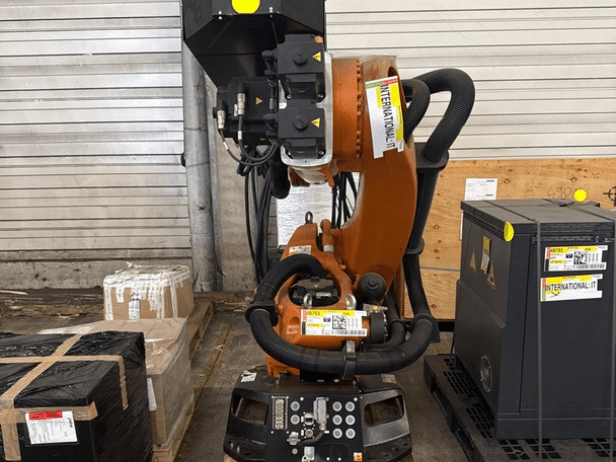 Дополнительный манипулятор робота KUKA KR 210 R2700 в виде спереди, представленный на поддоне рядом с упаковками и оборудованием.