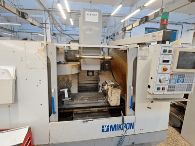 Фрезерный станок с ЧПУ Mikron VCE 750-2, вид спереди, панель управления и шпиндель в зоне обработки, видно износ и загрязнение.