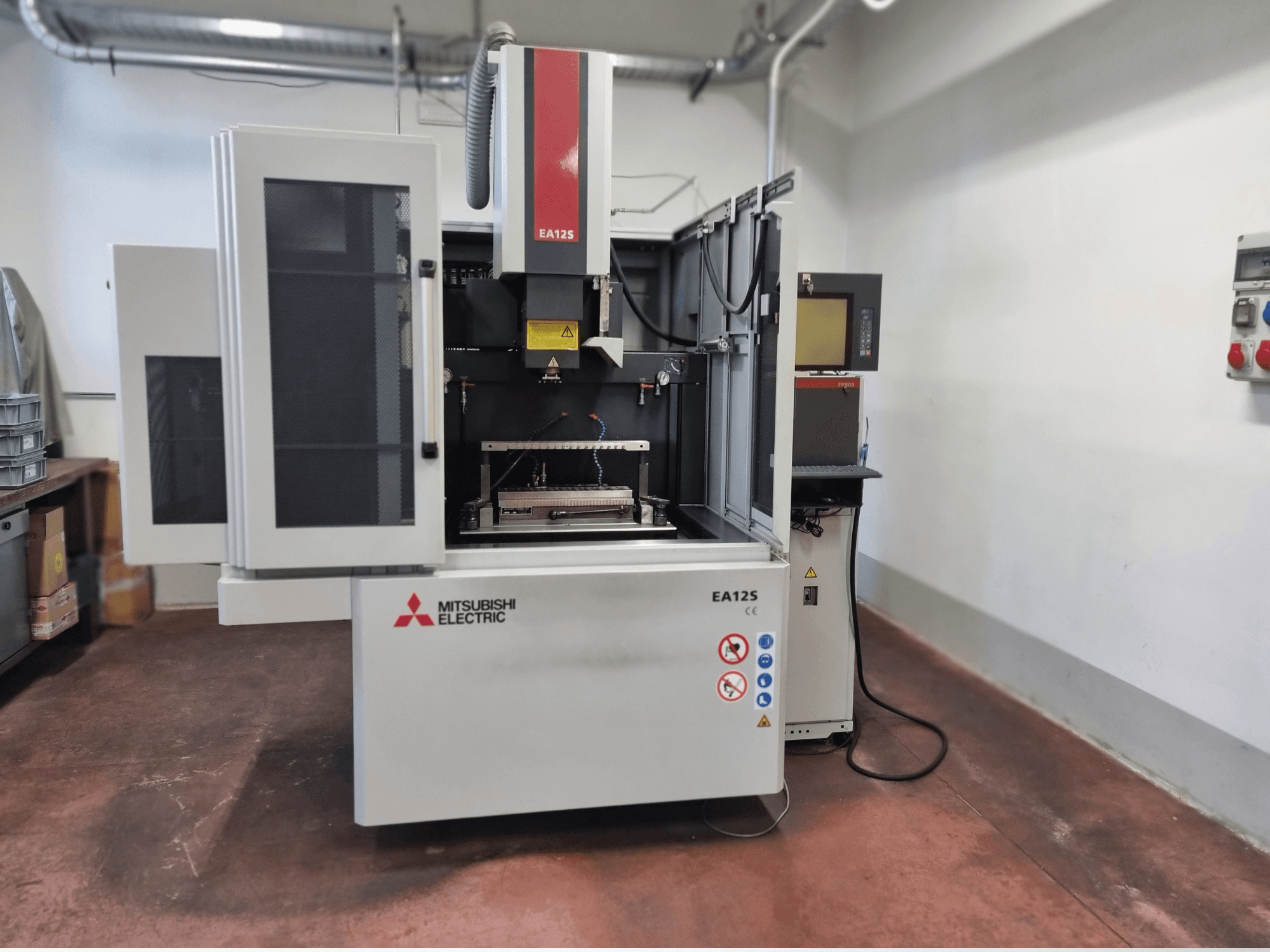 Станок для резки проволоки Mitsubishi Electric EA12S, вид спереди, открытые дверцы, панель управления и наклейки безопасности.