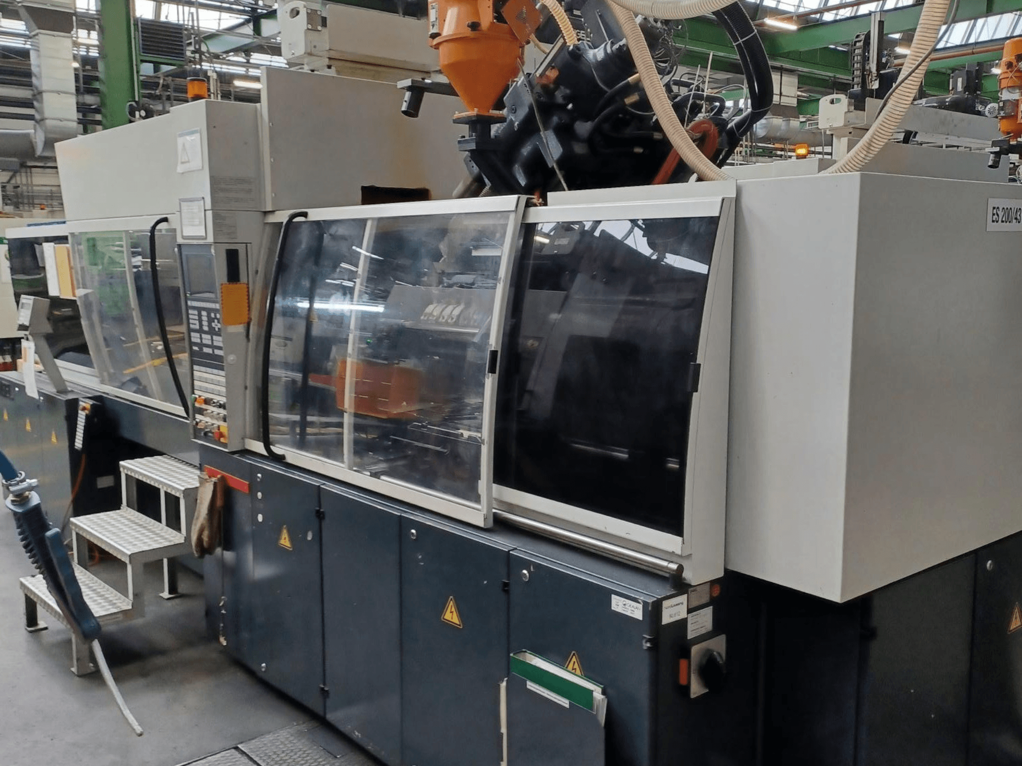 Вид спереди машины для литья пластмасс под давлением, марка и модель неизвестны, с прозрачными защитными дверцами и панелью управления.