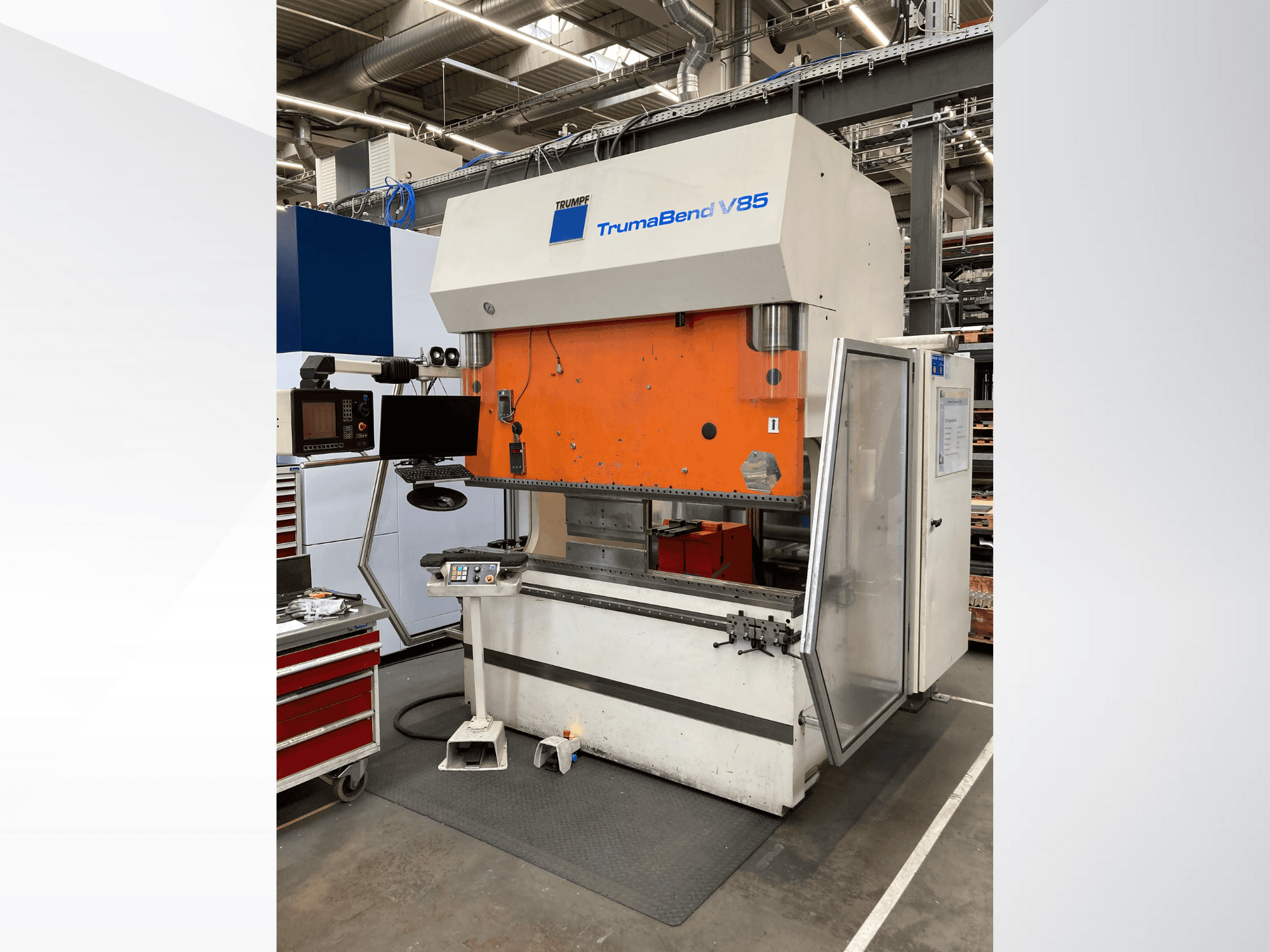 Гибочный станок TruMatic V85 на заводе, с оранжевой передней панелью, экраном управления и открытой боковой дверью, вид сбоку.