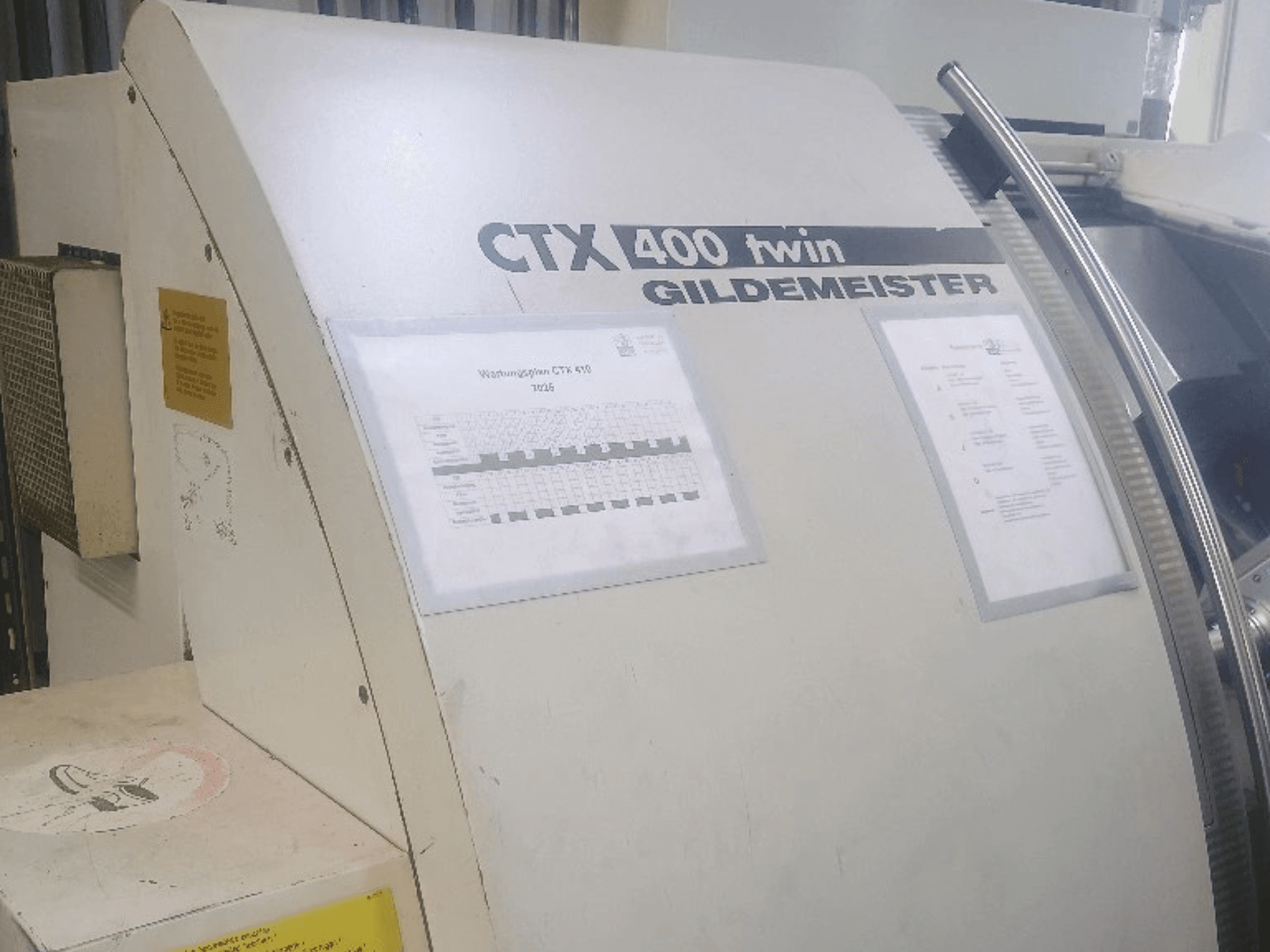 Двухшпиндельный горизонтальный токарный станок Gildemeister CTX 400, вид спереди, на котором видны панели управления и техническая документация.