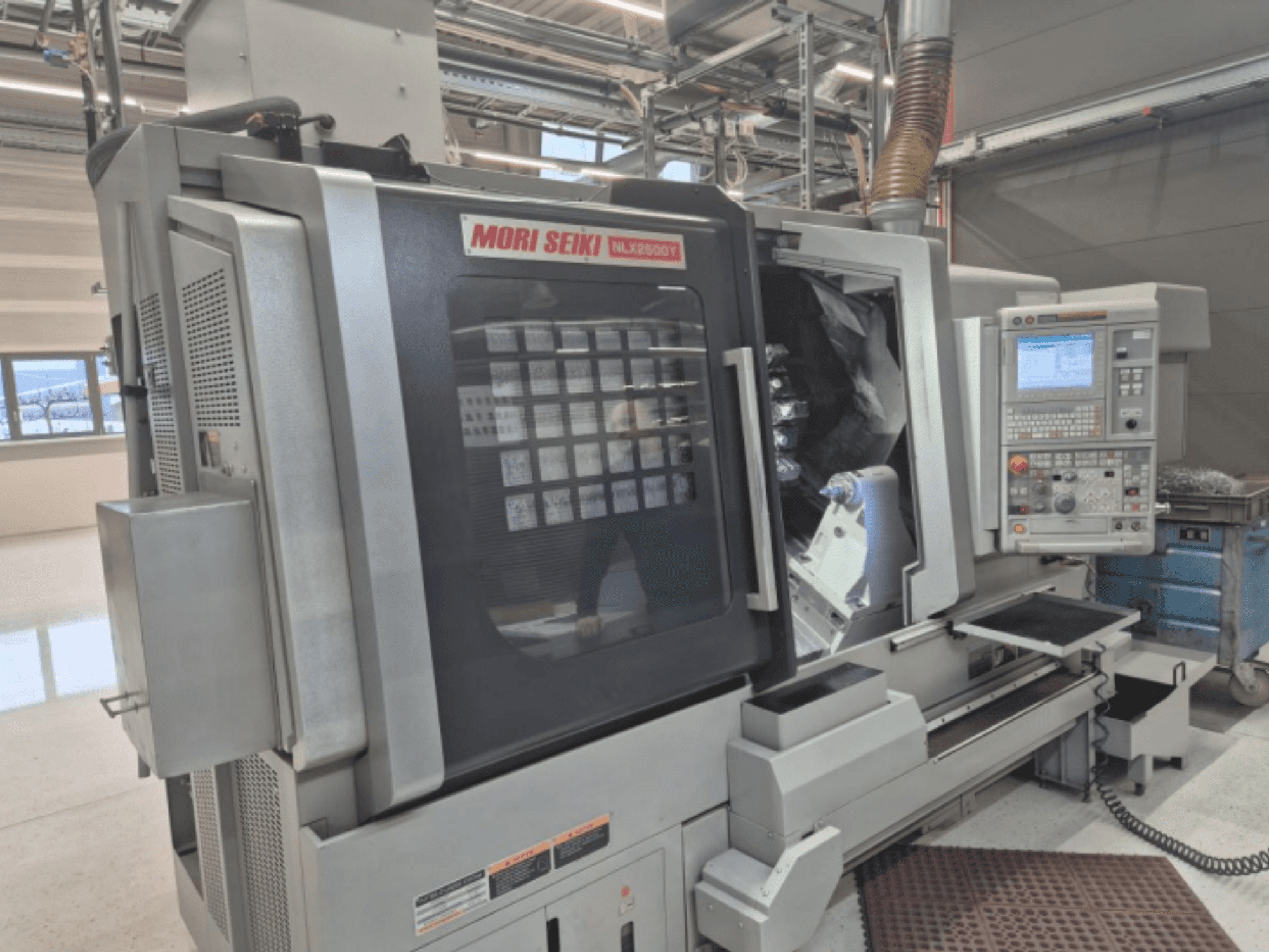 Токарный станок с ЧПУ MORI SEIKI NL2500Y в заводских условиях, вид спереди, демонстрирующий панель управления и камеру для заготовок.