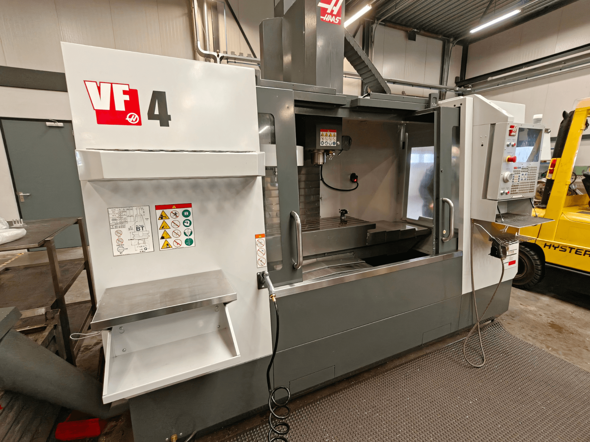 Вертикальный обрабатывающий центр HAAS VF-4, вид спереди, панель управления, рабочая зона и наклейки безопасности сбоку.