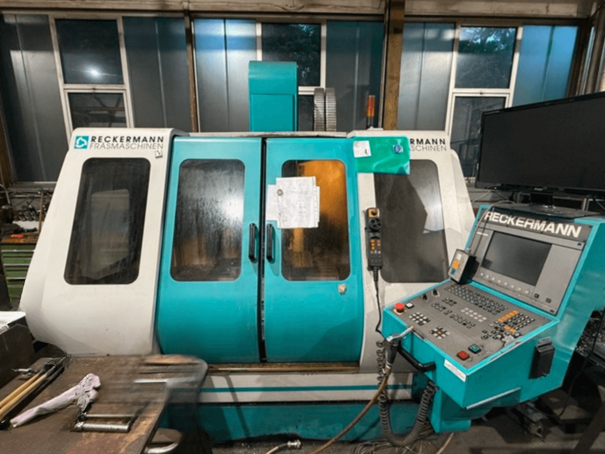 Универсальный обрабатывающий центр RECKERMANN VMC 850, вид спереди с изображением панели управления и стеклянных дверей.
