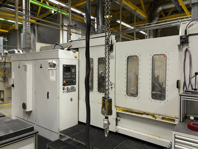 Промышленный станок с ЧПУ с панелью управления, вид сбоку; окна, цепи и металлические детали в заводских условиях.