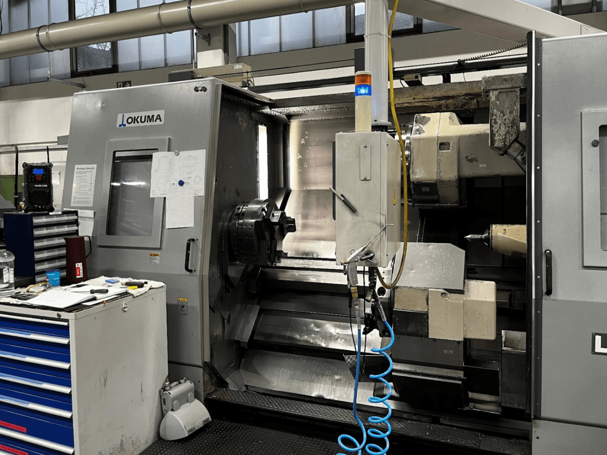 Горизонтальный токарный станок Okuma LU35-M, вид спереди. Панель управления, инструменты и большой патрон для обработки.