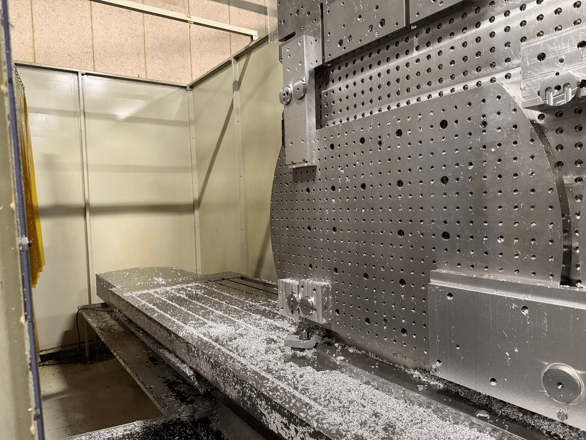 Крупный план переднего вида универсального обрабатывающего центра KIHEUNG KNC-U1000, на котором виден металлический рабочий стол с алюминиевой стружкой.