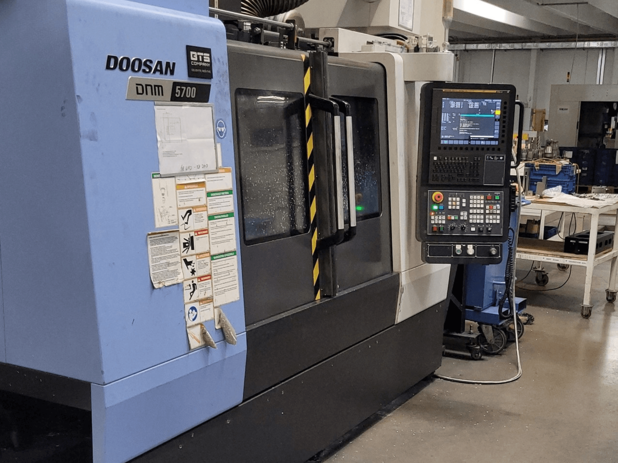 Вертикальный обрабатывающий центр DOOSAN DNM 5700, вид спереди, на котором видны панель управления и органы управления.